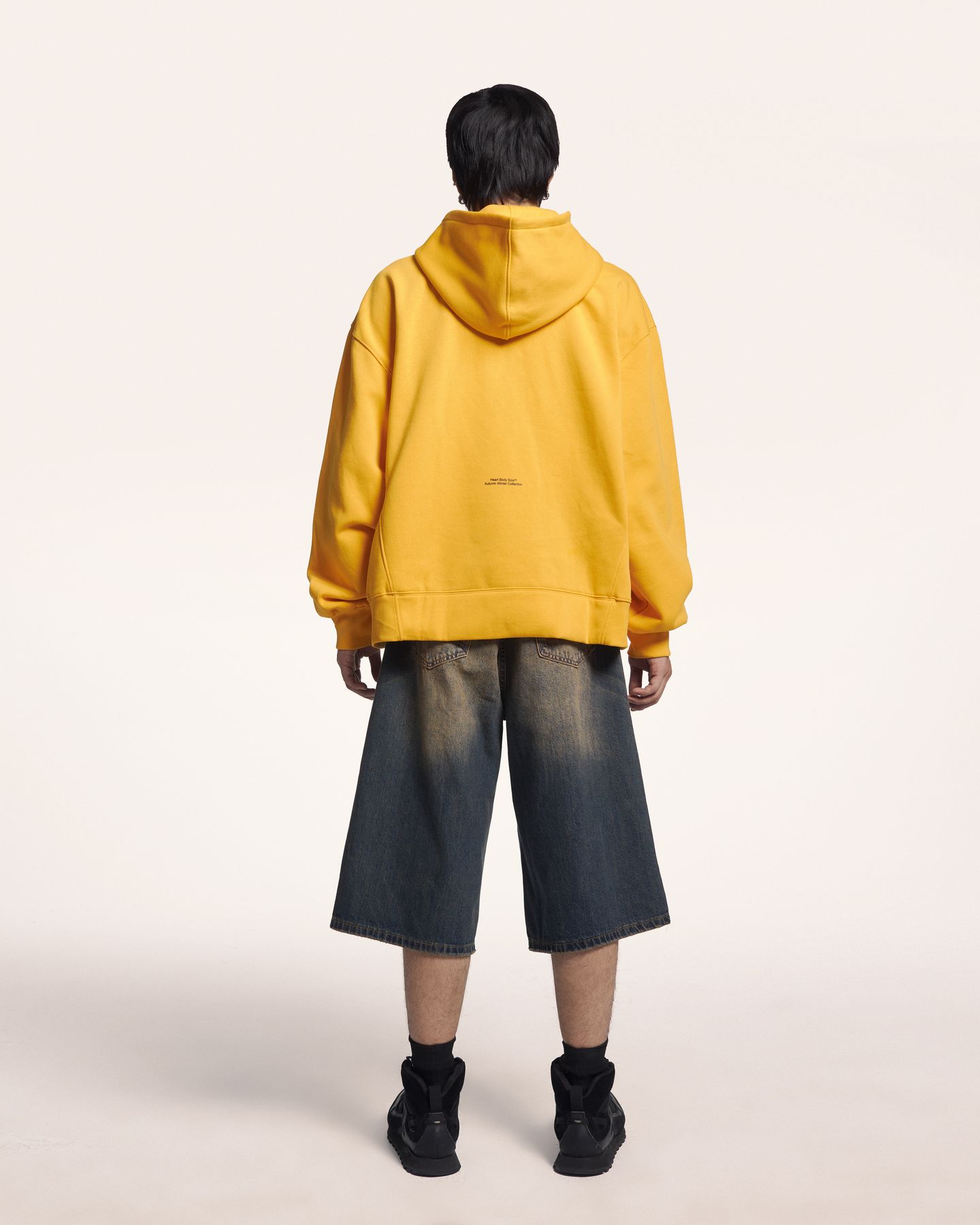Người mẫu quay lưng mặc hoodie vàng và quần short jean